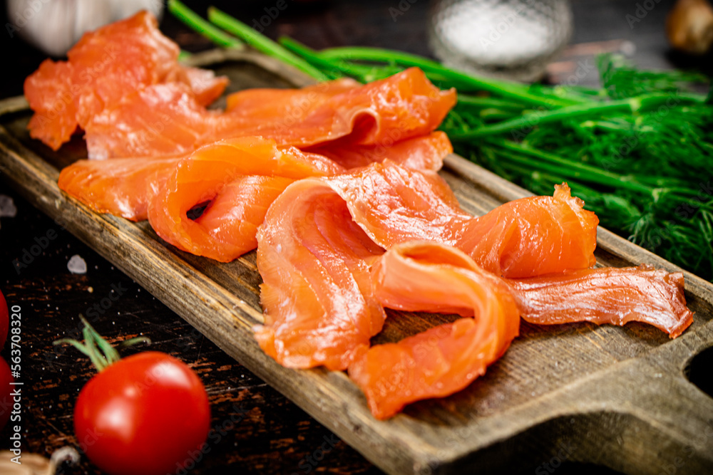 Slices of salted salmon on a cutting board with dill and tomatoes. Slices of salted salmon on a cutting board with dill and tomatoes.