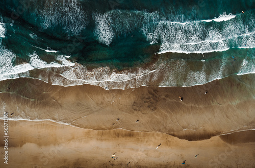 Top view by drone of yellow sand beach with ocean and waves. Beach with a lot of surfers and people on sunny day from above. © Matt Benzero