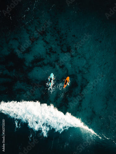 Photography Two surfers floating on surfboard in tropical ocean with big and powerful wave behind them