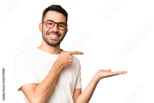 Young handsome caucasian man over isolated chroma key background holding copyspace imaginary on the palm to insert an ad