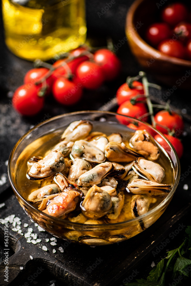 Pickled mussels in a bowl on a cutting board with cherry tomatoes. 