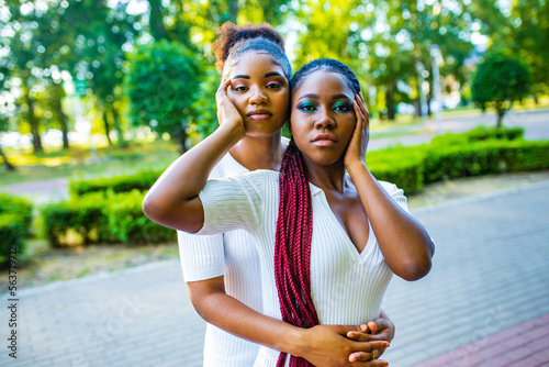 two afro american women celebrating marriage in wtite dress with bright male up in summer park photo