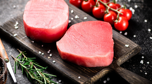 Fresh raw tuna on a cutting board with tomatoes, spices and rosemary. 