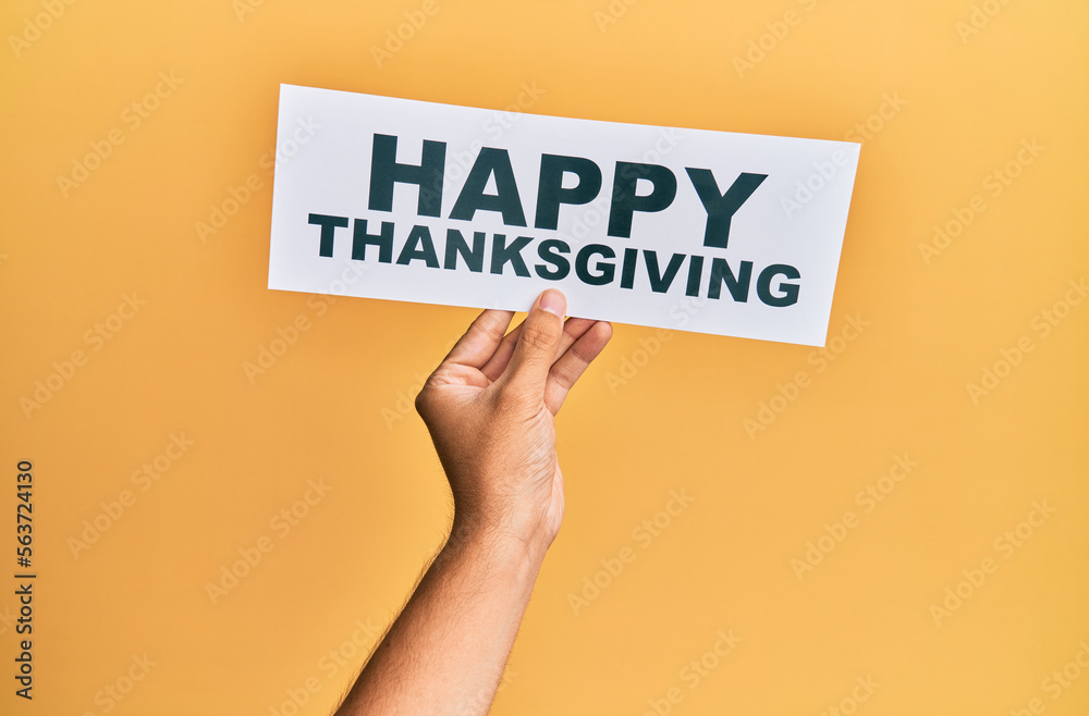 Hand of caucasian man holding paper with happy thanksgiving message over isolated yellow background Hand of caucasian man holding paper with happy thanksgiving message over isolated yellow background