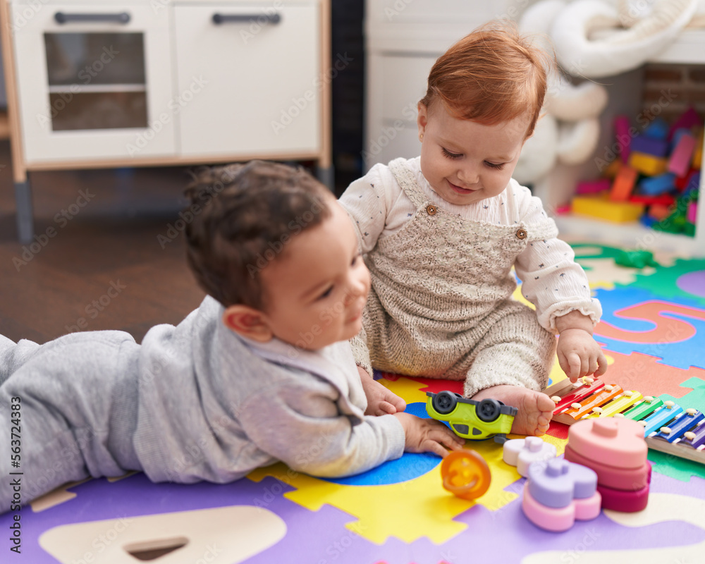 Obraz premium Two adorable babies playing with toys sitting on floor at kindergarten
