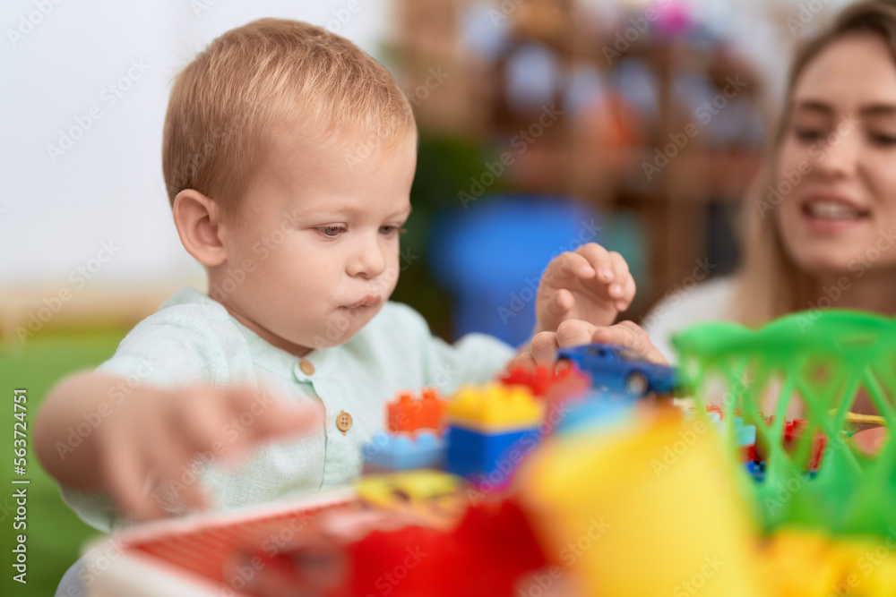 Teacher and toddler playing with construction blocks sitting on table at kindergarten Teacher and toddler playing with construction blocks sitting on table at kindergarten