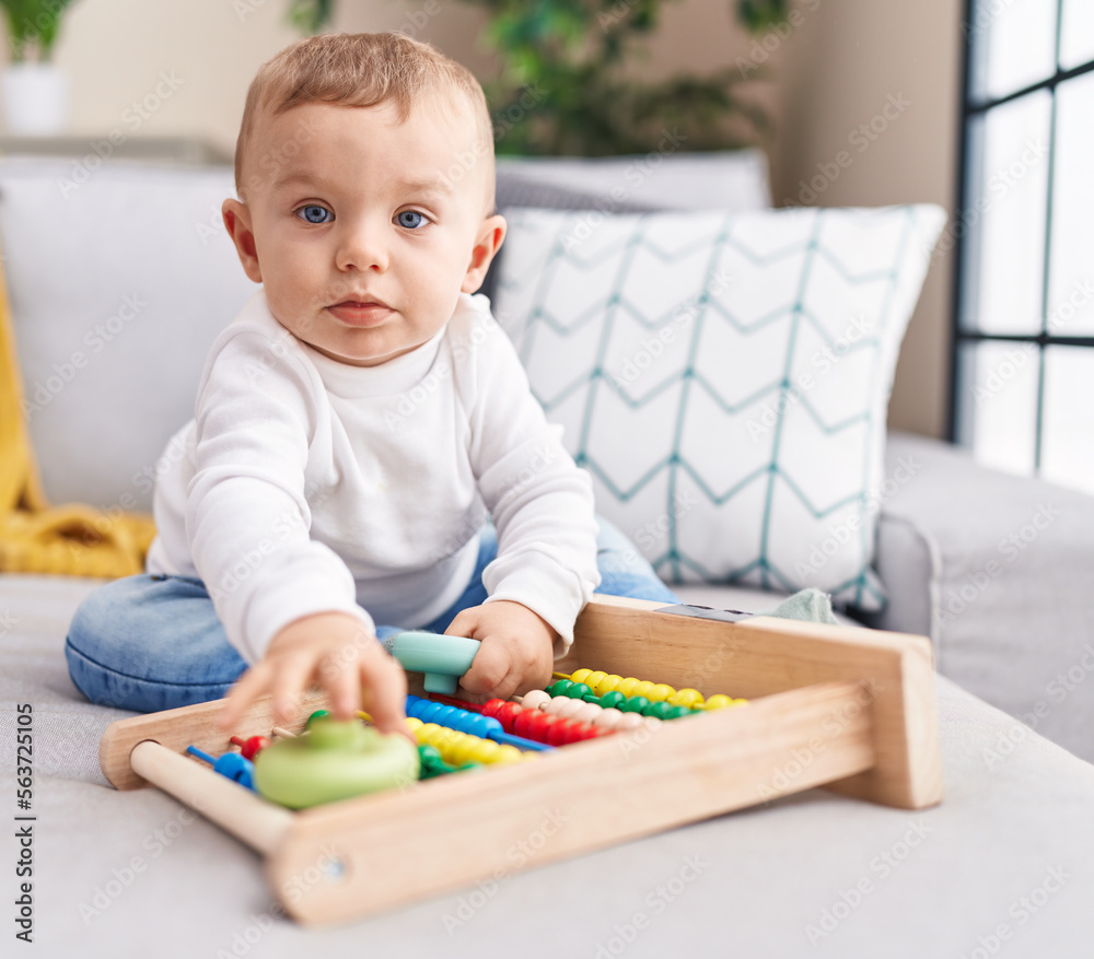 Adorable blond toddler playing with abacus sitting on sofa at home Adorable blond toddler playing with abacus sitting on sofa at home