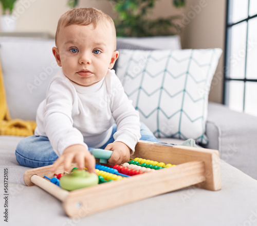 Adorable blond toddler playing with abacus sitting on sofa at home