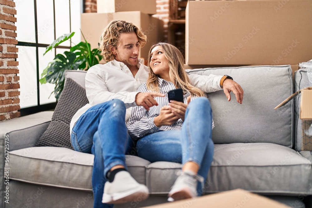 Man and woman couple using smartphone sitting on sofa at new home Man and woman couple using smartphone sitting on sofa at new home