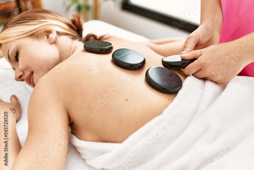 Young caucasian woman lying on table having back massage using hot stones at beauty salon