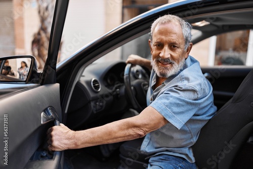 Fototapet Senior grey-haired man smiling confident opening car door at street