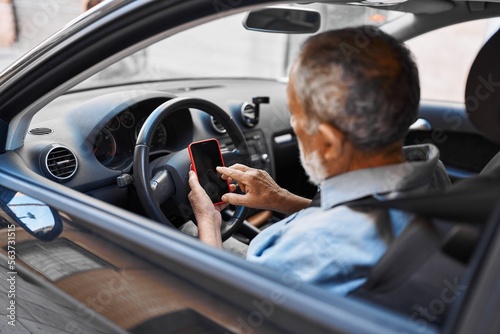 Senior grey-haired man using smartphone sitting on car at street © Krakenimages.com