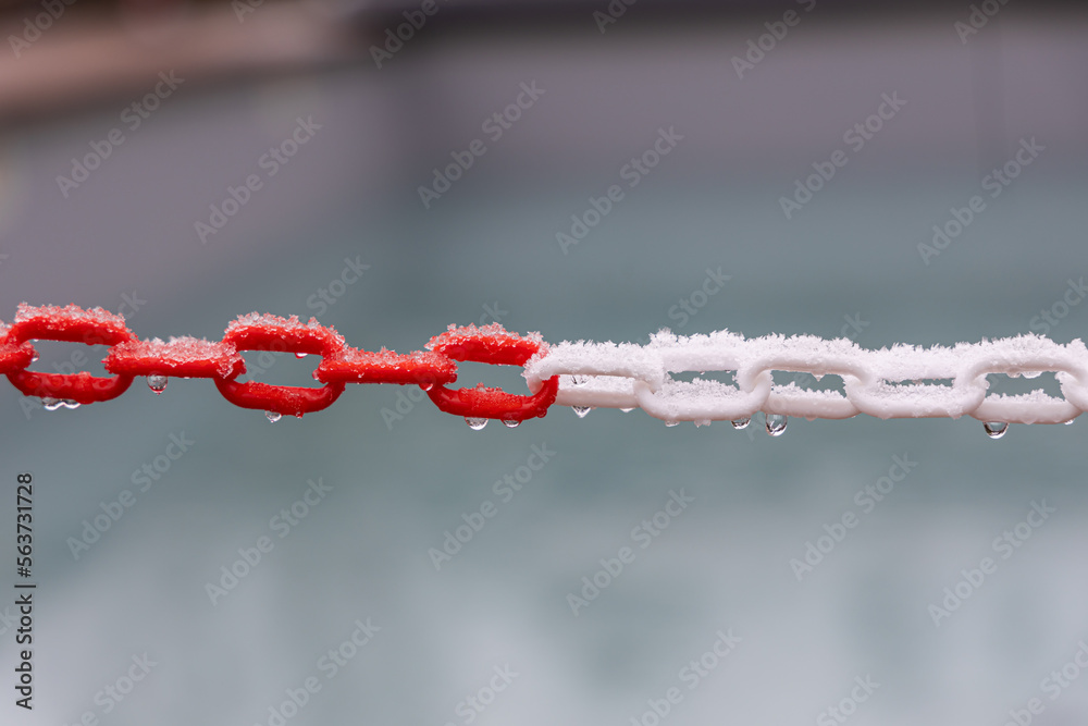 Red and white plastic chain with snow and water drops outdoors in autumn Red and white plastic chain with snow and water drops outdoors in autumn