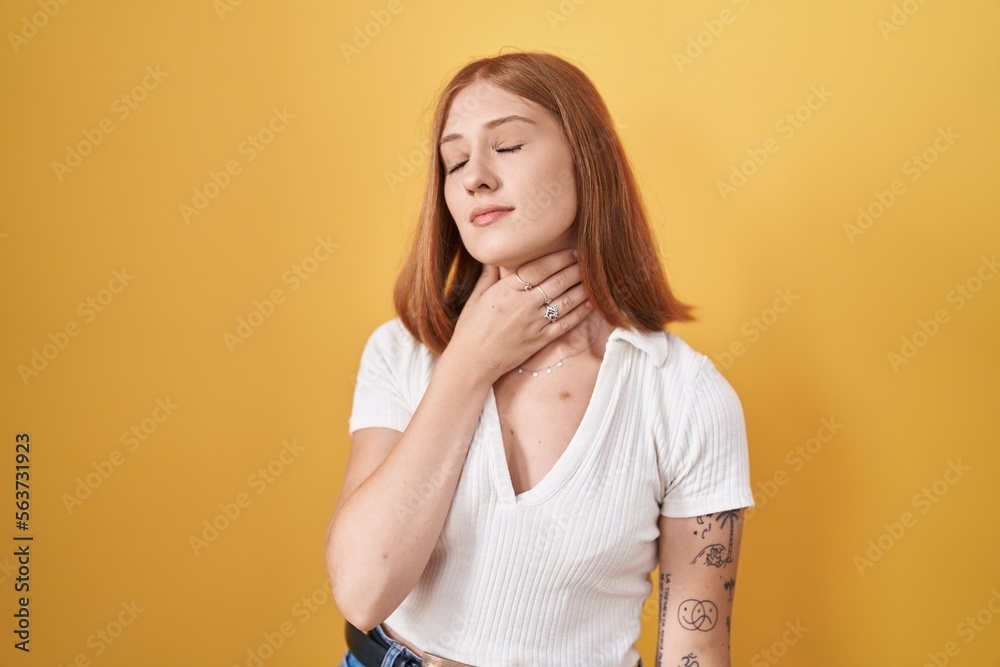 Young redhead woman standing over yellow background touching painful neck, sore throat for flu, clod and infection Young redhead woman standing over yellow background touching painful neck, sore throat for flu, clod and infection