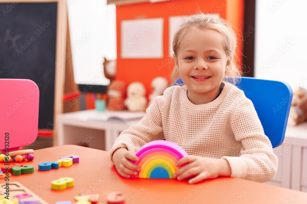 Adorable blonde girl playing with toys sitting on table at kindergarten Adorable blonde girl playing with toys sitting on table at kindergarten