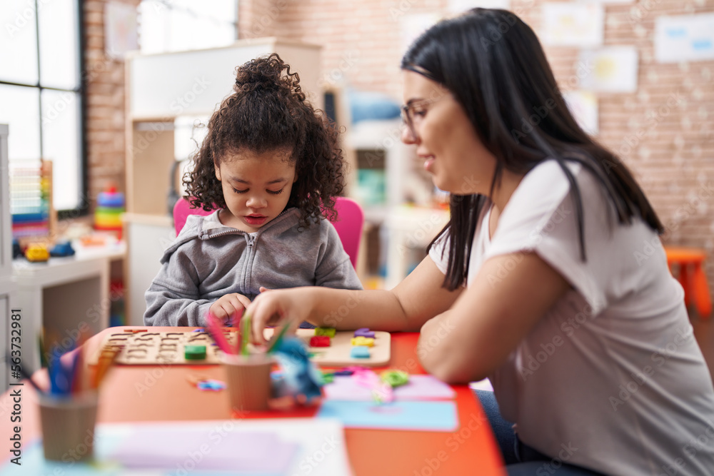 Teacher and toddler playing with maths puzzle game sitting on table at kindergarten Teacher and toddler playing with maths puzzle game sitting on table at kindergarten