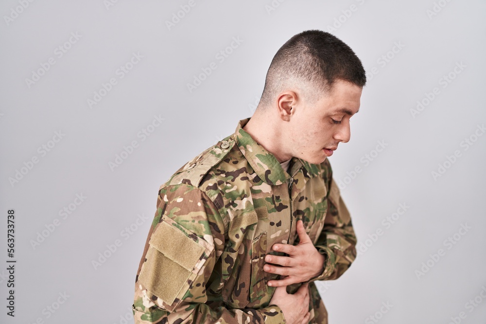 Young man wearing camouflage army uniform with hand on stomach because nausea, painful disease feeling unwell. ache concept.