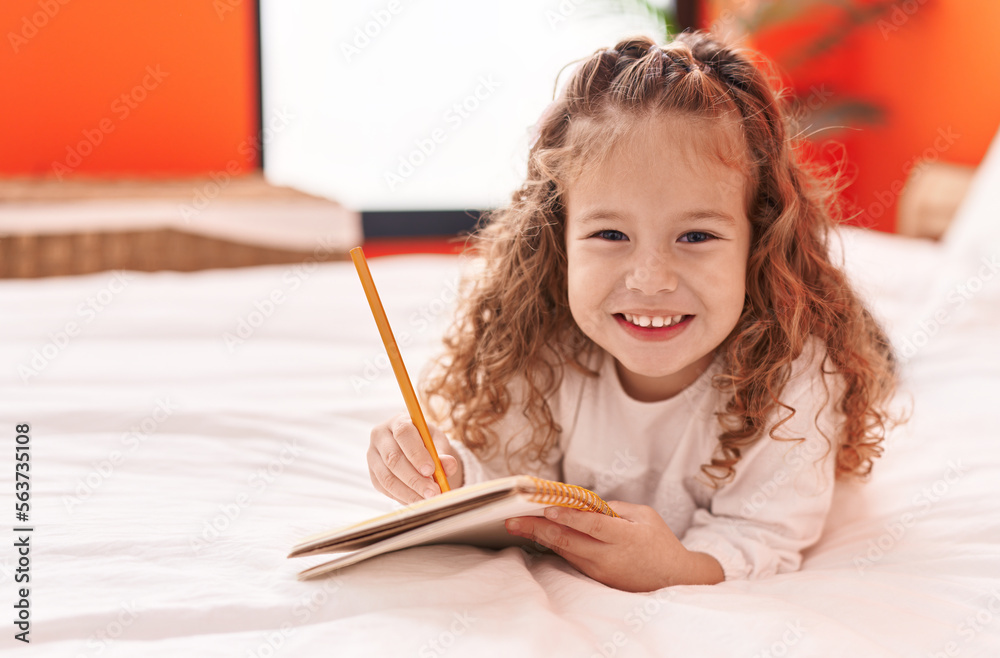 Adorable blonde toddler writing on notebook lying on bed at bedroom Adorable blonde toddler writing on notebook lying on bed at bedroom