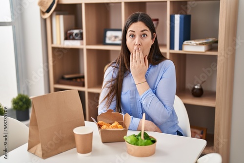 Young brunette woman eating take away food at home covering mouth with hand  shocked and afraid for mistake. surprised expression