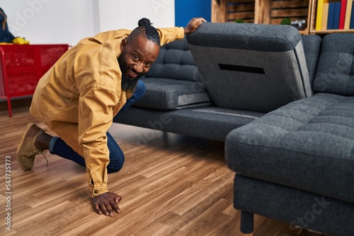 Young african american man looking for something under sofa at home © Krakenimages.com