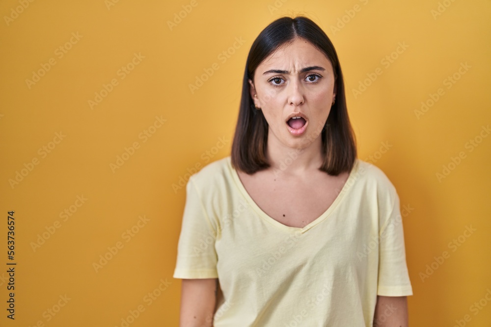 Hispanic girl wearing casual t shirt over yellow background in shock face, looking skeptical and sarcastic, surprised with open mouth Hispanic girl wearing casual t shirt over yellow background in shock face, looking skeptical and sarcastic, surprised with open mouth