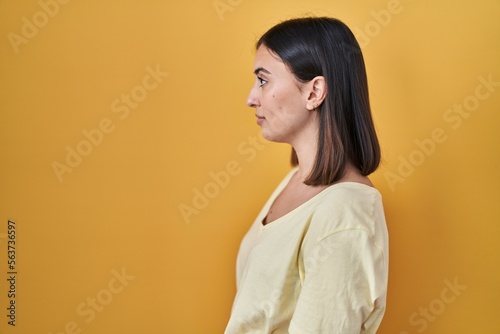 Hispanic girl wearing casual t shirt over yellow background looking to side, relax profile pose with natural face and confident smile.