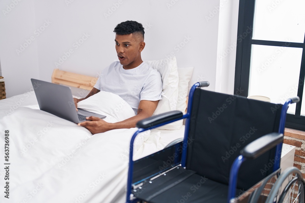 Young hispanic man lying on the bed, using wheelchair scared and amazed with open mouth for surprise, disbelief face Young hispanic man lying on the bed, using wheelchair scared and amazed with open mouth for surprise, disbelief face