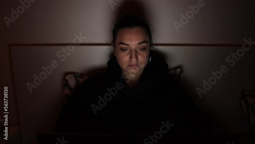 A girl in bed in a dark room working on a notebook 