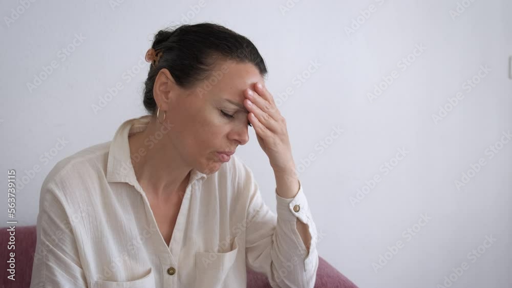 Female feel head spasms on sofa. An upset woman with a strong headpain sitting in loneliness on the sofa in the flat. Female feel head spasms on sofa. An upset woman with a strong headpain sitting in loneliness on the sofa in the flat.