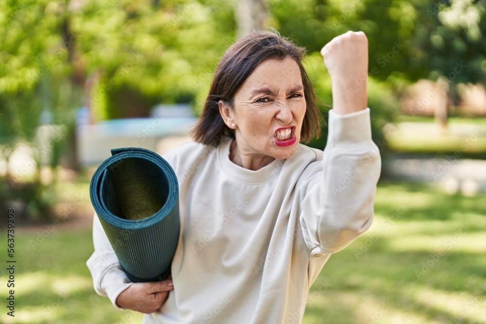 Middle age hispanic woman holding yoga mat at the park annoyed and frustrated shouting with anger, yelling crazy with anger and hand raised Middle age hispanic woman holding yoga mat at the park annoyed and frustrated shouting with anger, yelling crazy with anger and hand raised