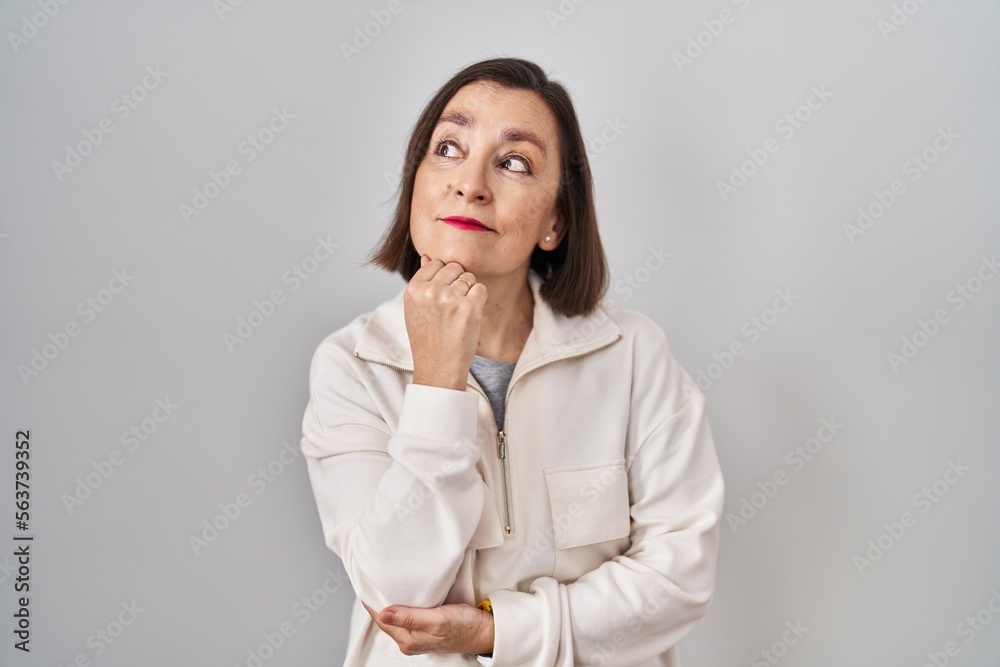 Middle age hispanic woman standing over isolated background with hand on chin thinking about question, pensive expression. smiling with thoughtful face. doubt concept.
