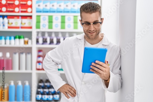 Young caucasian man pharmacist using touchpad working at pharmacy