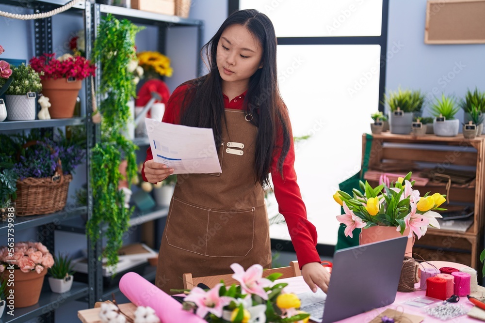 Young chinese woman florist using laptop reading document at flower shop