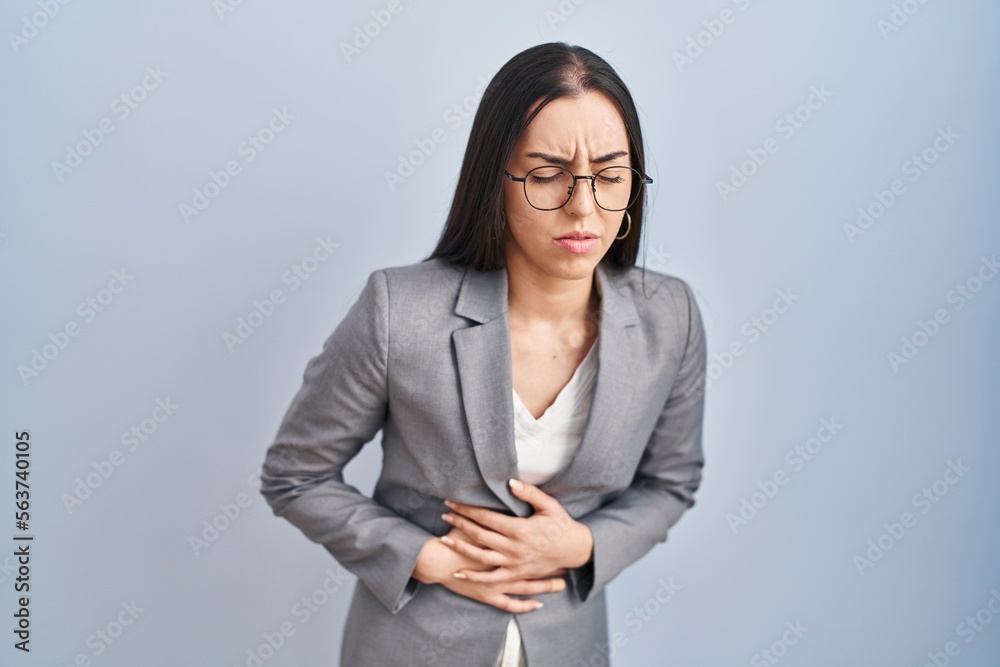 Hispanic business woman wearing glasses with hand on stomach because nausea, painful disease feeling unwell. ache concept.