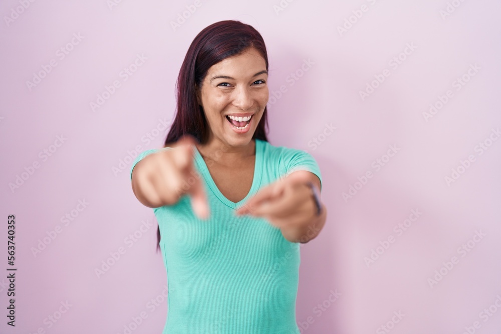 Young hispanic woman standing over pink background pointing to you and the camera with fingers, smiling positive and cheerful Young hispanic woman standing over pink background pointing to you and the camera with fingers, smiling positive and cheerful