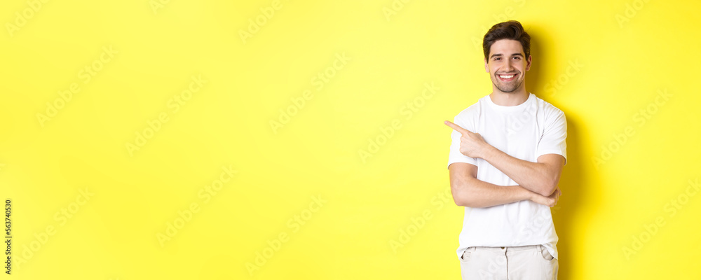 Handsome guy pointing left and smiling, showing advertisement on yellow copy space - obrazy, fototapety, plakaty 