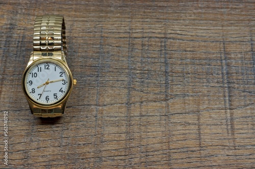 Gold watch at eight thirteen on a wooden counter top
