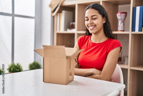 Young brazilian woman looking inside cardboard box happy face smiling with crossed arms looking at the camera. positive person.