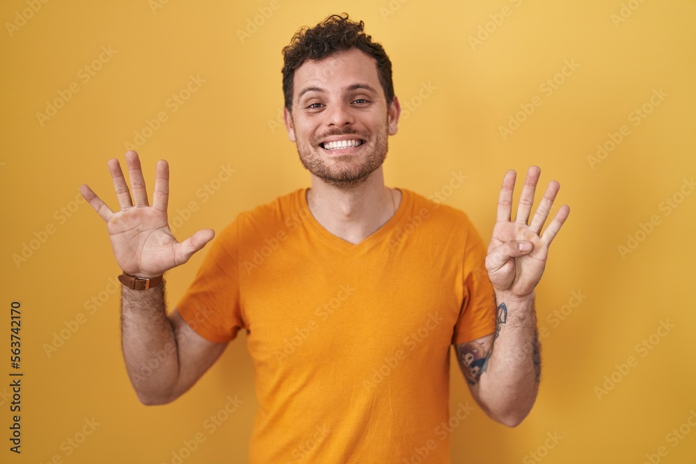 Young hispanic man standing over yellow background showing and pointing up with fingers number nine while smiling confident and happy. Young hispanic man standing over yellow background showing and pointing up with fingers number nine while smiling confident and happy.