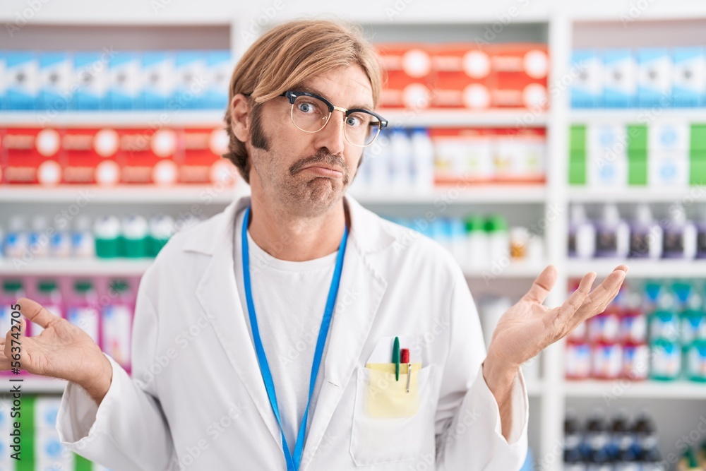 Caucasian man with mustache working at pharmacy drugstore clueless and confused expression with arms and hands raised. doubt concept. Caucasian man with mustache working at pharmacy drugstore clueless and confused expression with arms and hands raised. doubt concept.