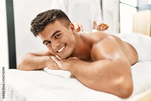 Young hispanic man smiling confident having skin back treatment at beauty center