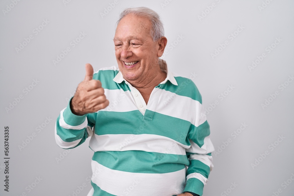 Senior man with grey hair standing over white background looking proud, smiling doing thumbs up gesture to the side Senior man with grey hair standing over white background looking proud, smiling doing thumbs up gesture to the side