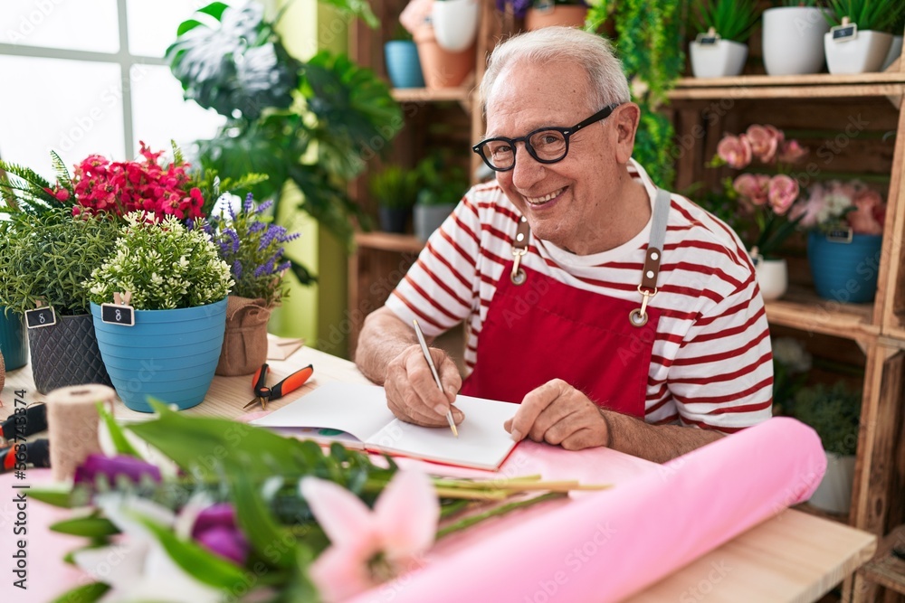 Middle age grey-haired man florist smiling confident writing on notebook at flower shop