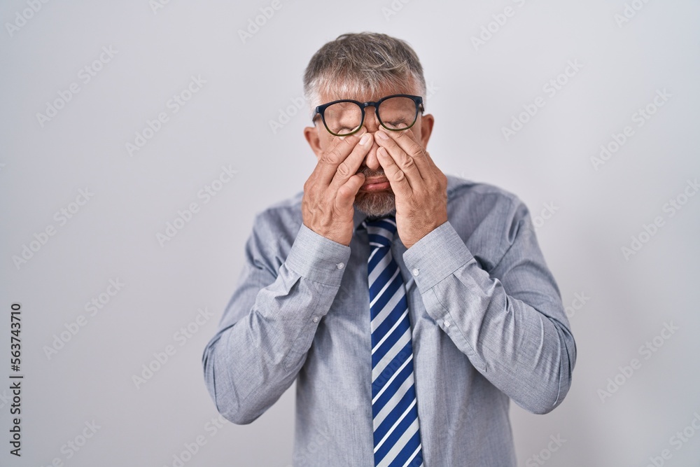 Hispanic business man with grey hair wearing glasses rubbing eyes for fatigue and headache, sleepy and tired expression. vision problem Hispanic business man with grey hair wearing glasses rubbing eyes for fatigue and headache, sleepy and tired expression. vision problem