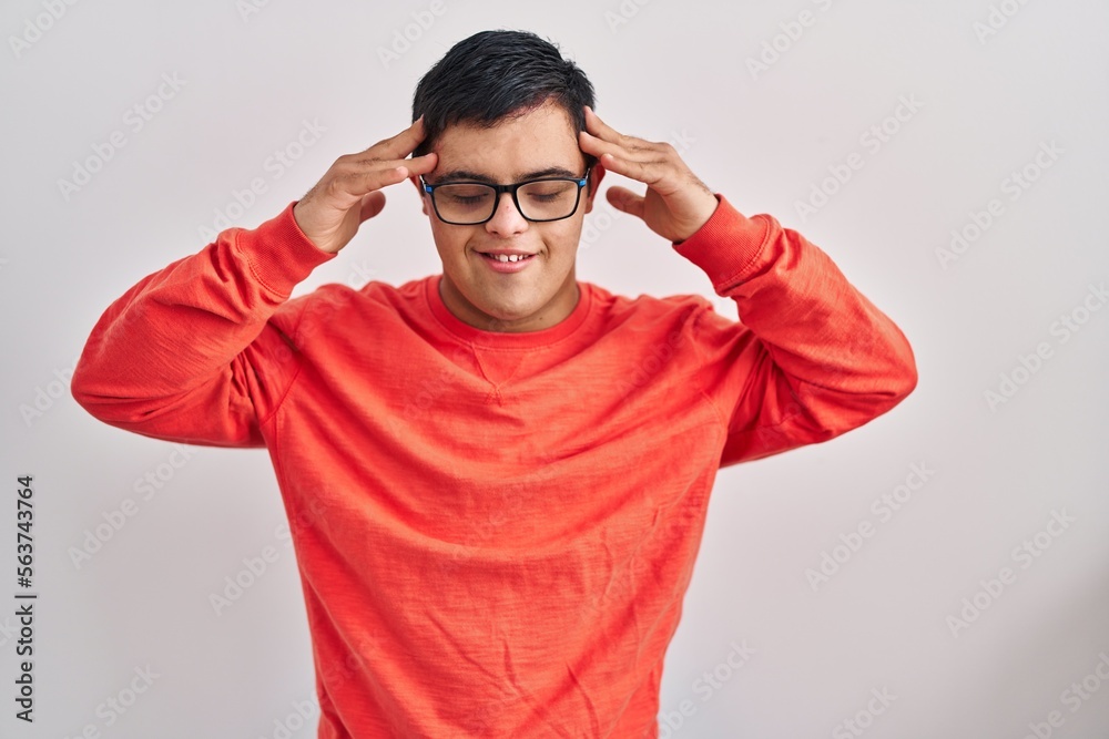 Young hispanic man with down syndrome standing over white background with hand on head, headache because stress. suffering migraine. Young hispanic man with down syndrome standing over white background with hand on head, headache because stress. suffering migraine.