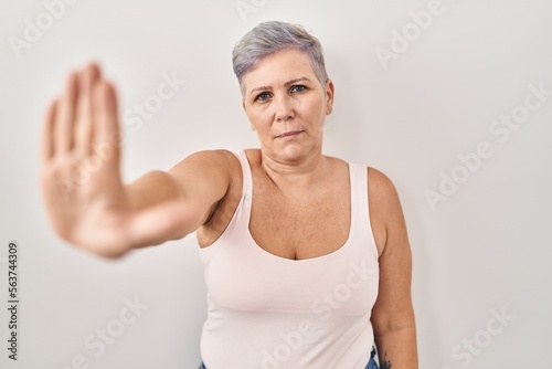 Middle age caucasian woman standing over white background doing stop sing with palm of the hand. warning expression with negative and serious gesture on the face.