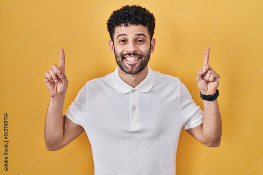 Arab man standing over yellow background smiling amazed and surprised and pointing up with fingers and raised arms. Arab man standing over yellow background smiling amazed and surprised and pointing up with fingers and raised arms.