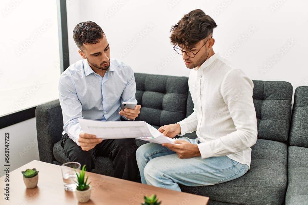 Two hispanic men business workers reading document working at office Two hispanic men business workers reading document working at office