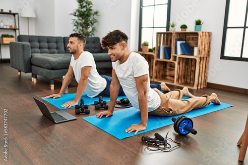 Two hispanic men couple smiling confident having online stretching class at home