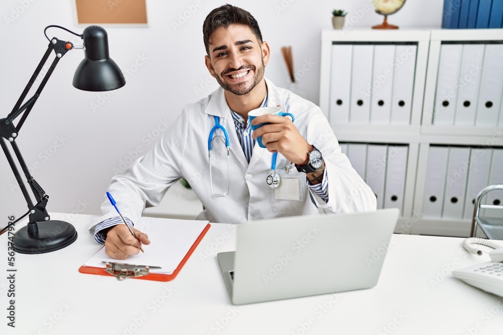 Handsome hispanic man working as doctor drinking a coffee at medical consultation Handsome hispanic man working as doctor drinking a coffee at medical consultation